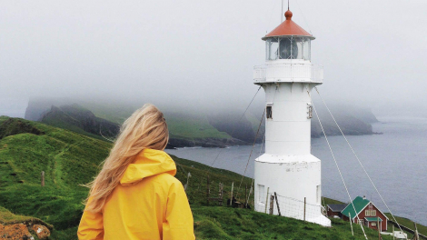 View of a woman looking at a lighthouse in the Faroe Islands